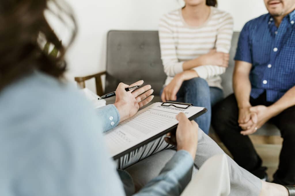 Padres firmando un acuerdo de custodia compartida consensuado en un entorno de mediación familiar con menores, priorizando su bienestar.