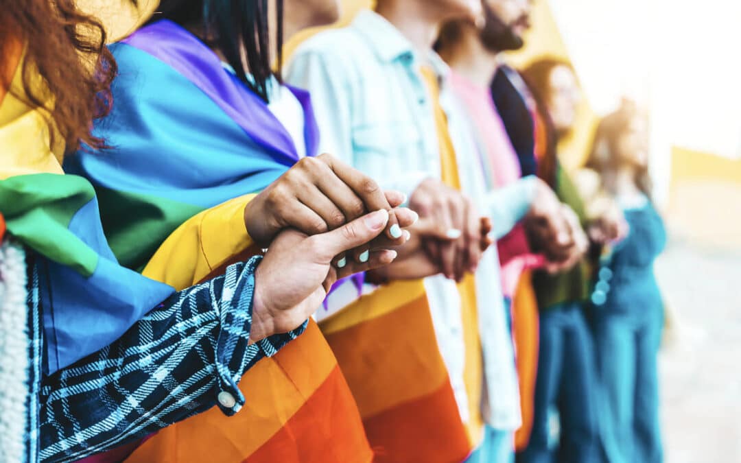 Grupo de personas de diferentes edades y orígenes sosteniendo una cuerda de colores, en representación de la diversidad, la inclusión y el colectivo LGTBIQ+.
