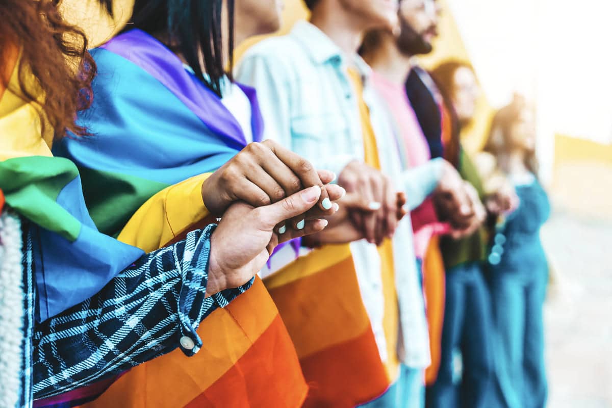 Grupo de personas de diferentes edades y orígenes sosteniendo una cuerda de colores, en representación de la diversidad, la inclusión y el colectivo LGTBIQ+.