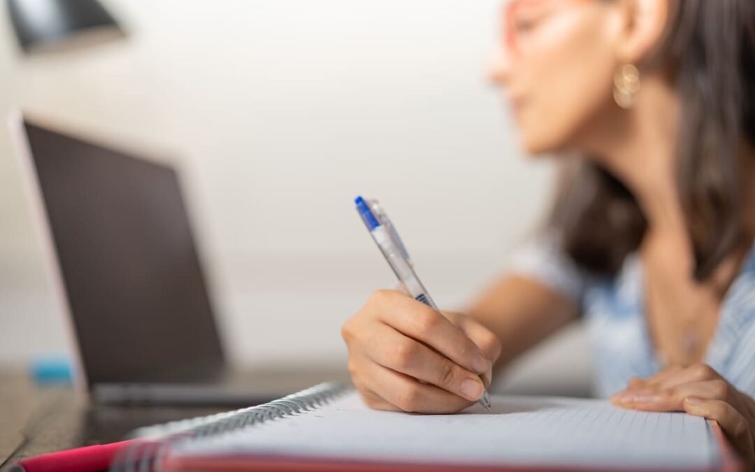 Alumna tomando apuntes mientras consulta los requisitos para hacer un máster online.