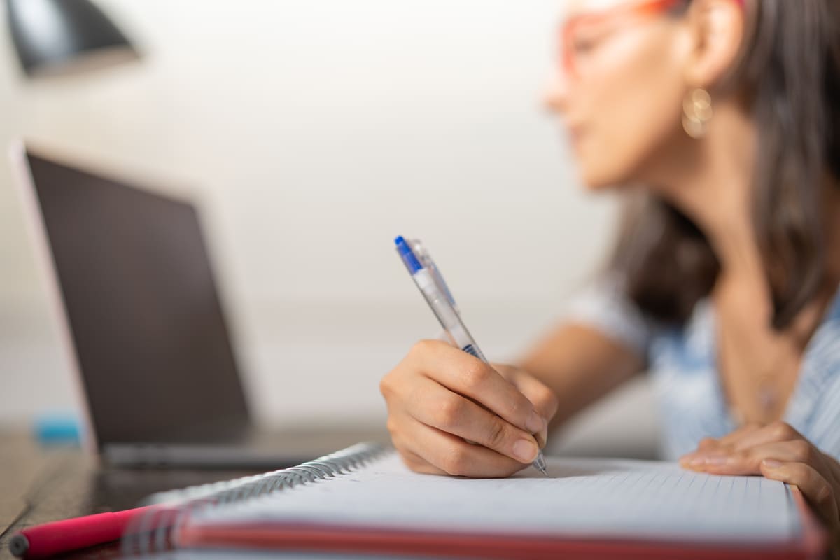 Alumna tomando apuntes mientras consulta los requisitos para hacer un máster online.